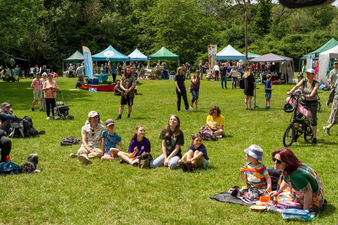Image of people sitting on green grass listening to music with stalls in the background